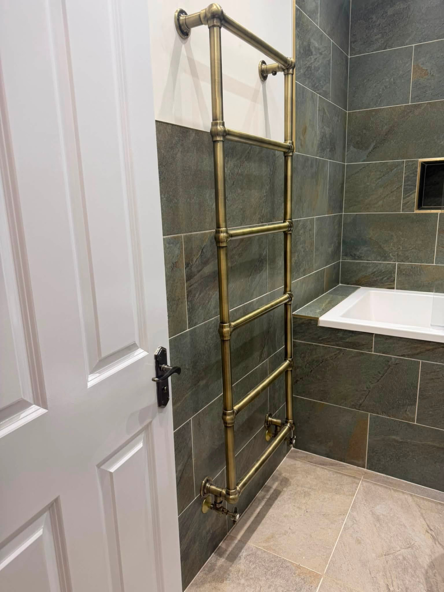 Antique brass heated towel ladder against slate tiling